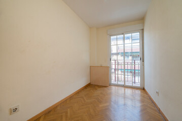 Empty room with light cream painted walls, herringbone oak parquet floor and balcony with white aluminum sliding doors