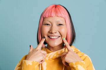 Wall Mural - Asian girl with pink hair and piercing pointing fingers at her smile