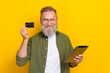 Portrait of positive aged man hold debit plastic card tablet toothy smile isolated on yellow color background