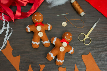 Two figurines of a gingerbread man made of felt made by hand against a background of wood and tools