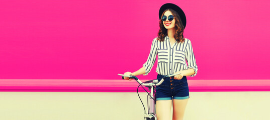 Summer colorful portrait of happy smiling young woman with bicycle in the city on pink background