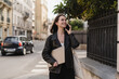 © LIGHTFIELD STUDIOS - cheerful freelancer in black leather jacket holding laptop and talking on smartphone on street in paris.