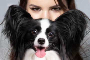 A cute young woman is hugging her papillon puppy. The eyes of a beautiful girl and the eyes of a funny dog with big ears.