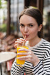 © LIGHTFIELD STUDIOS - portrait of woman in striped long sleeve shirt holding glass and drinking orange juice in outdoor cafe in paris.