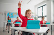 © Halfpoint - Happy schoolgirl with hands up using digital tablet during lesson in classroom at primary school.