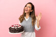 © luismolinero - Young woman holding birthday cake over isolated pink background saluting with hand with happy expression