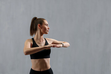 Young sporty woman in sports clothes stretching arms against grey background, copy space