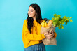 © luismolinero - Young woman holding a grocery shopping bag isolated on blue background looking to the side and smiling