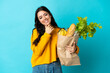 © luismolinero - Young woman holding a grocery shopping bag isolated on blue background happy and smiling