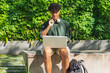 © ADDICTIVE STOCK - Ethnic male student with laptop in park