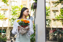 Asian Woman With Flowers In Pots Looking At Shop Window