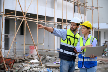 Wall Mural - Young attractive construction man and woman in vest with helmet working with laptop on building construction site. Home building project. Engineer foreman discusses with a coworker at workplace.