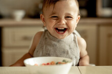 Cute Smiling Baby Eats Colorful Cereal Flakes For Breakfast. The Child Is Happy, He Is Sincerely Happy And Smiling