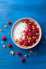 Wall Mural - Bowl with fresh greek yogurt, raspberries and walnut on blue table top view. Healthy diet breakfast.