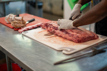 Wall Mural - A close up of a large prime rib roast which is sitting on a brown plastic cutting board. The meat has some marbling and multiple ribs. The chef is using a long knife to cut steaks from the fresh meat.