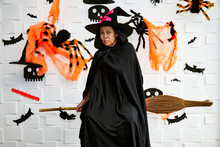 Halloween Wizard And Witch Concept - Senior Woman In Witch Costumes Celebrating Halloween Posing On Broom With Bats And Spider Web Over White Background
