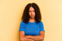 Young Brazilian Woman Isolated On Yellow Background Frowning Face In Displeasure, Keeps Arms Folded.