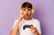 Young hispanic man playing with a video game controller isolated on purple background pointing temple with finger, thinking, focused on a task.