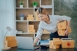 © Kritdanai - Looking camera, Startup small business SME, Entrepreneur owner using tablet taking receive and checking online purchase shopping order to preparing pack product box