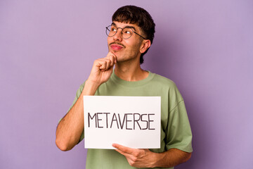 Young hispanic man holding metaverse placard isolated on purple background looking sideways with doubtful and skeptical expression.