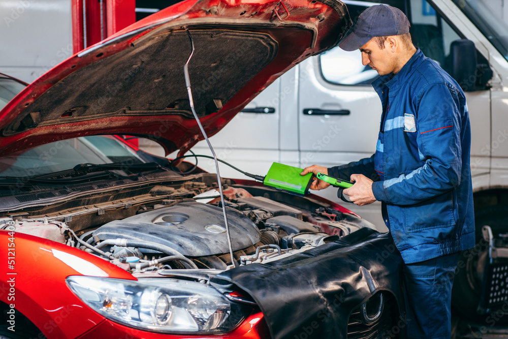 Car service electrician or mechanic uses a tablet computer with futuristic interactive diagnostics software. Inspecting the vehicle in order to find broken components in the engine bay of modern car