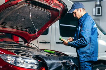 Car service electrician or mechanic uses a tablet computer with futuristic interactive diagnostics software. Inspecting the vehicle in order to find broken components in the engine bay of modern car