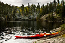 A Single Kayak Pulled Up On The Rocky Shore On A Small Lake In Northern Ontario. The Trees Are Showing Their Fall Colours And There Is A Little Dusting Of Snow. 