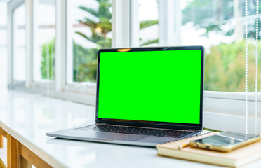 Wall Mural - Mockup of laptop computer with empty screen with notebook,ice coffee and smartphone on table side the window in the coffee shop at the cafe,Green screen