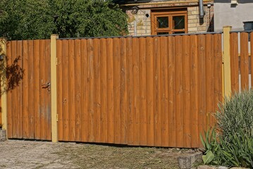 Canvas Print - closed brown rural wooden gate and door made of planks on the street on a green vegetation