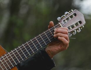 Hands of an adult man playing an acoustic guitar on the street, in a park close-up, selective focus. A man is playing an old acoustic guitar on the street. A street musician. Composer.	