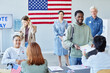 © Seventyfour - Diverse group of people in line at voting station focus on smiling black man receiving ballot form, copy space