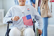 © Seventyfour - Closeup of young woman in wheelchair holding American flag after voting on election day, copy space