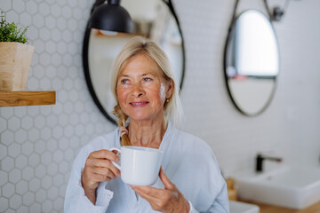 Poster - Beautiful senior woman in bathrobe drinking tea in bathroom, relax and wellness concept.