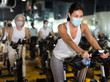 Portrait of young adult woman wearing face mask for disease protection training on stationary bike workout in gym