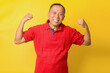 © Gatot - Asian pensioner grandpa raise two hands show muscles wear red t-shirt isolated yellow color background