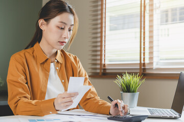 Wall Mural - Asian young employee, business woman calculate tax income and expenses, bills, credit card for payment or payday on table at home office. Financial, finance people concept.