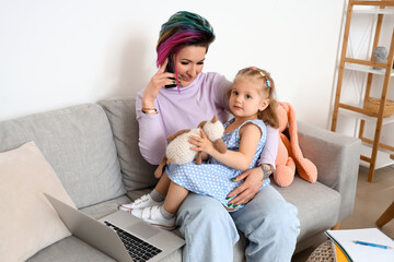 Wall Mural - Little girl with toy and her mother talking by mobile phone on sofa at home