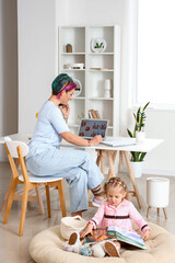 Wall Mural - Little girl with book and her working mother at home