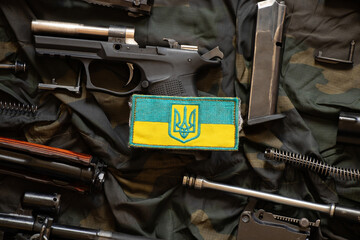 the patch of the flag of ukraine lies on a disassembled machine gun on a green camouflage fabric, wa