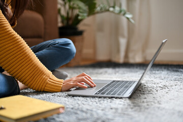 A young female sits on the comfy carpet and using portable laptop computer. cropped