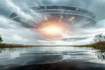 Wall Mural - ufo, an alien saucer hovering above the lake in the clouds, hovering motionless in the sky. unidenti
