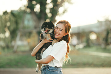 Wall Mural - Happy asian woman playing with dog on the park in sunset light, summer vacation.