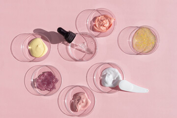 Wall Mural - Multicolored texture of cream, scrub and gel with a pipette in a Petri dish on a pink background. The concept of laboratory research of cosmetics. Smears of cosmetic skin care products