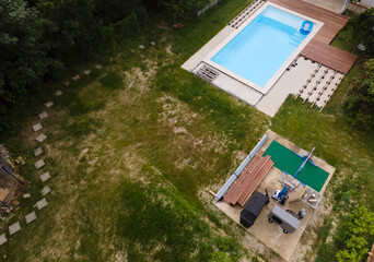 Wall Mural - Drone flight over beautiful green garden with pool and the wooden terrace of the pool is currently in progress