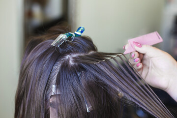 The hairdresser paints a brunette woman's hair in the beauty salon.