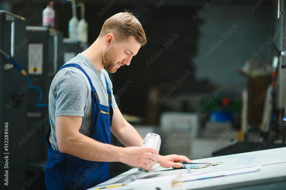 Man worker measuring printing color with spectrometer on the operating desk of the printing plant