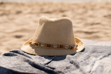 Chapeau de paille orné de coquillage, placé sur une serviette de plage. Été chaud. Protection du corps et de la tête. Vacances, soleil, plage et détente. Place pour le texte.