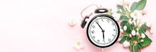 Black Alarm Clock That Shows 7 O'clock On A Pink Background With Apple Tree Spring Summer Flowers With Copy Space.