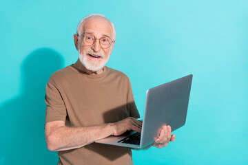 Sticker - Portrait of attractive cheery grey-haired man holding in hands using laptop isolated over bright blue color background