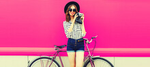Summer Image Of Happy Smiling Young Woman Photographer Taking Picture By Film Camera With Bicycle In The City On Pink Background